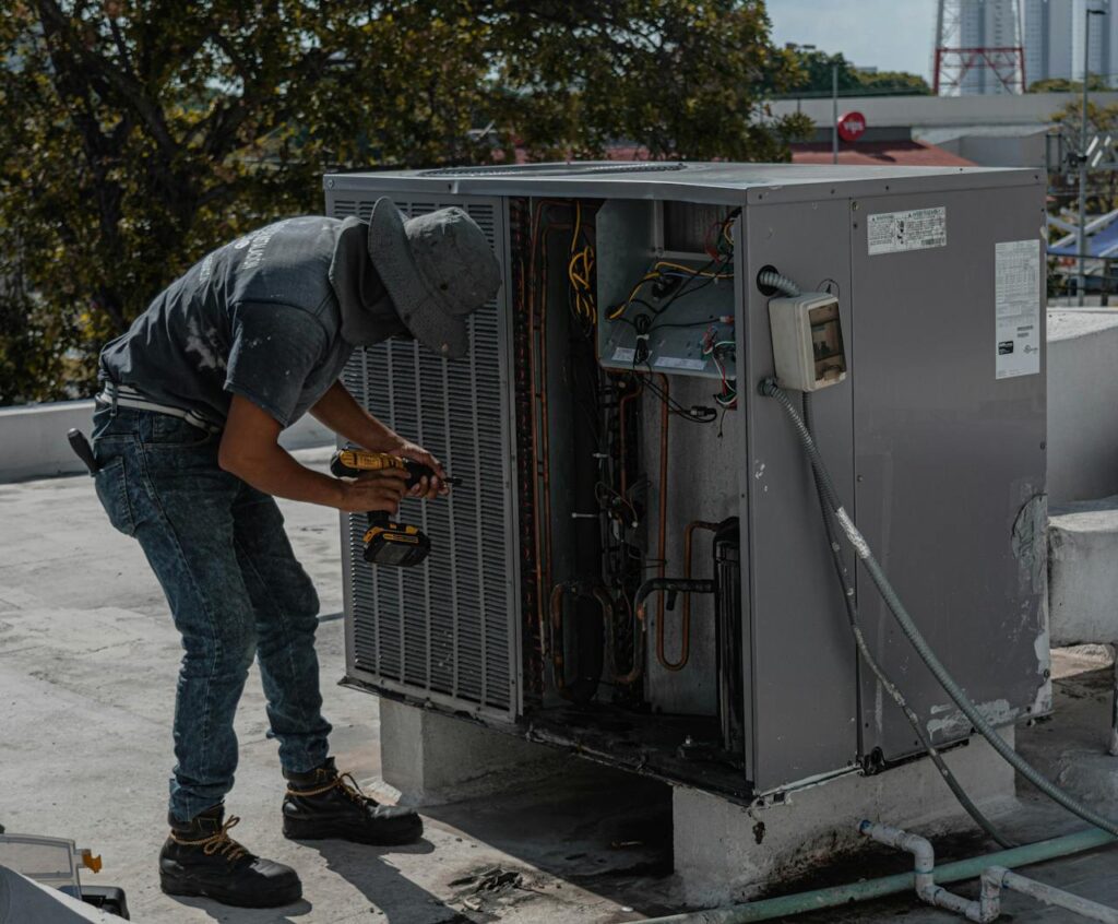 Professional Electrician Eldoradopark 078 564 3757 A worker in a bucket hat repairs an outdoor air conditioning unit on a rooftop.